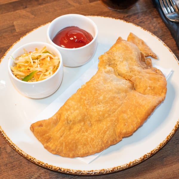 A golden-brown Caribbean fried bake with coleslaw and ketchup on a white plate.