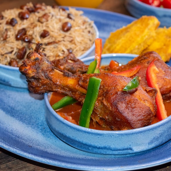 Paolo's Caribbean Fusion jerk chicken with rice and peas, plantains, and peppers on a blue plate.