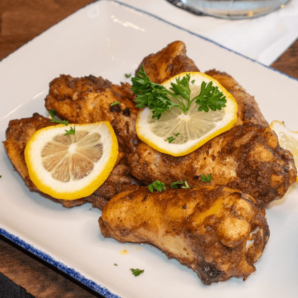 Paolo's Caribbean Fusion chicken wings, garnished with lemon slices and fresh parsley on a white plate.