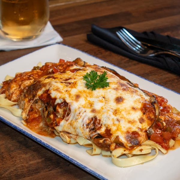 Paolo's Caribbean Fusion's cheesy baked pasta with red sauce and parsley garnish, with a drink and fork.