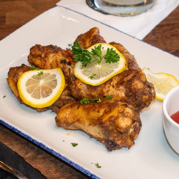 Paolo's Caribbean Fusion chicken wings, garnished with lemon slices and parsley on a white plate.