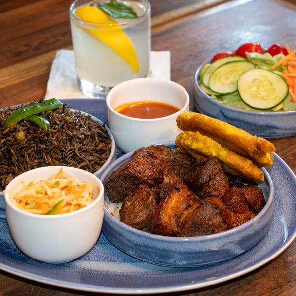 Paolo's Caribbean Fusion meal with dark rice, fried plantains, meat, salad, and a drink.
